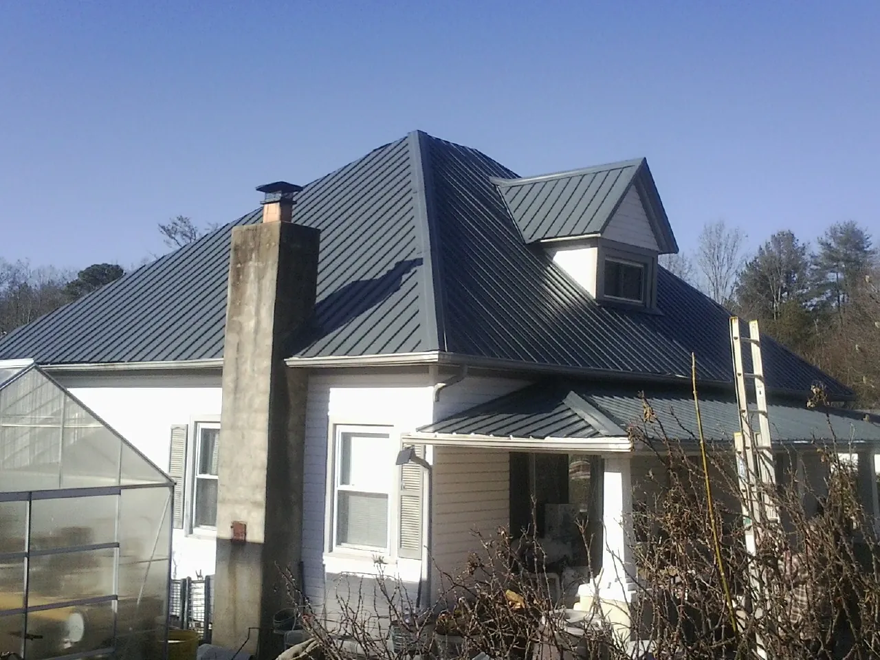 Dark blue standing seam metal roof on a white farmhouse with dormer — Slate & Tile Roof Repair by Roofing Brothers in Moravia