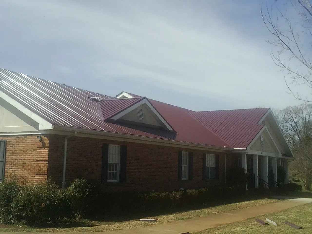 Red metal roof with gabled entries on a long brick building, from a Hail Damage Roof Repair job in Moravia