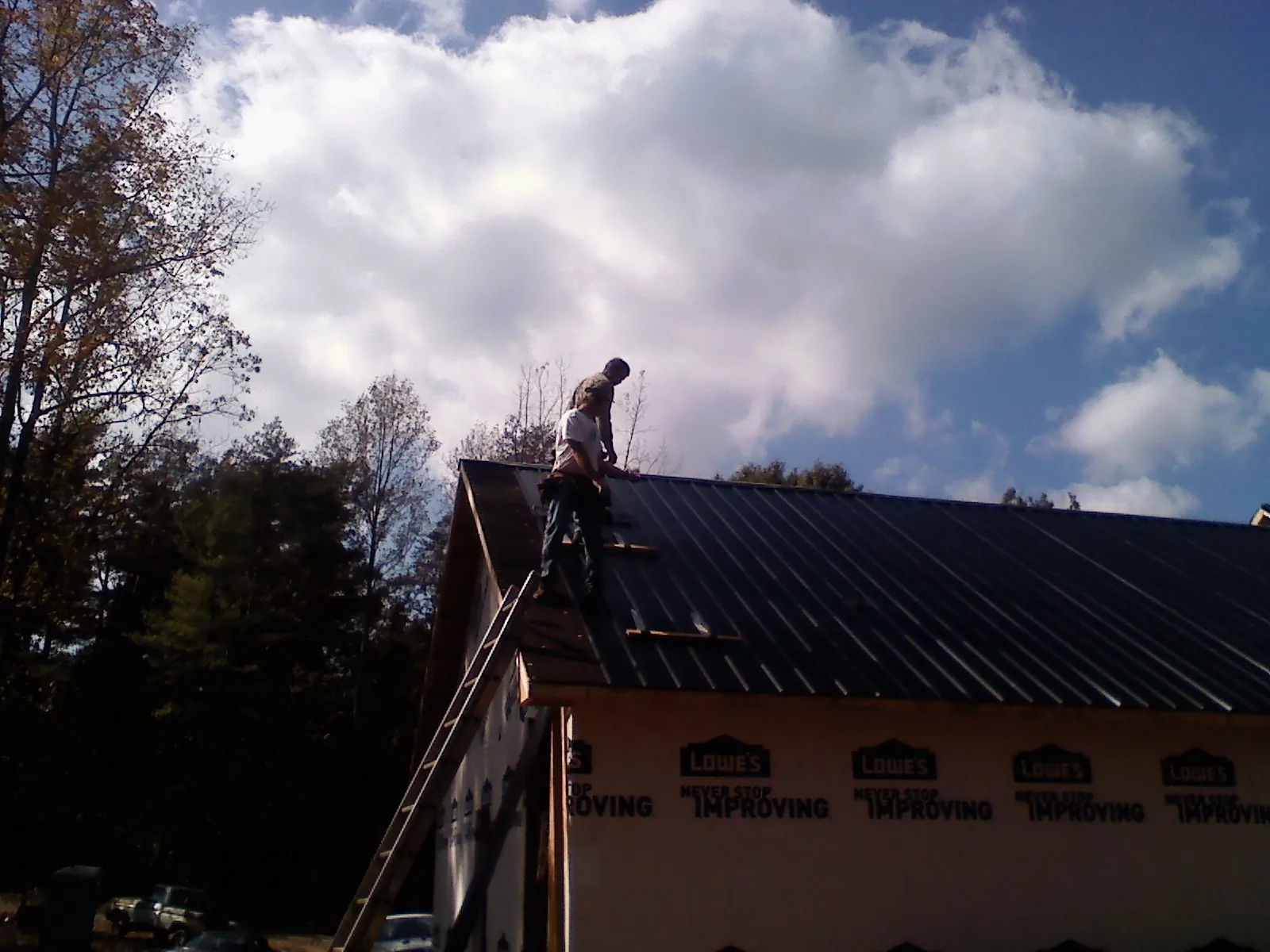 Roofer fastening dark metal panels high against a cloudy sky, from a Roof Inspection job in Moravia