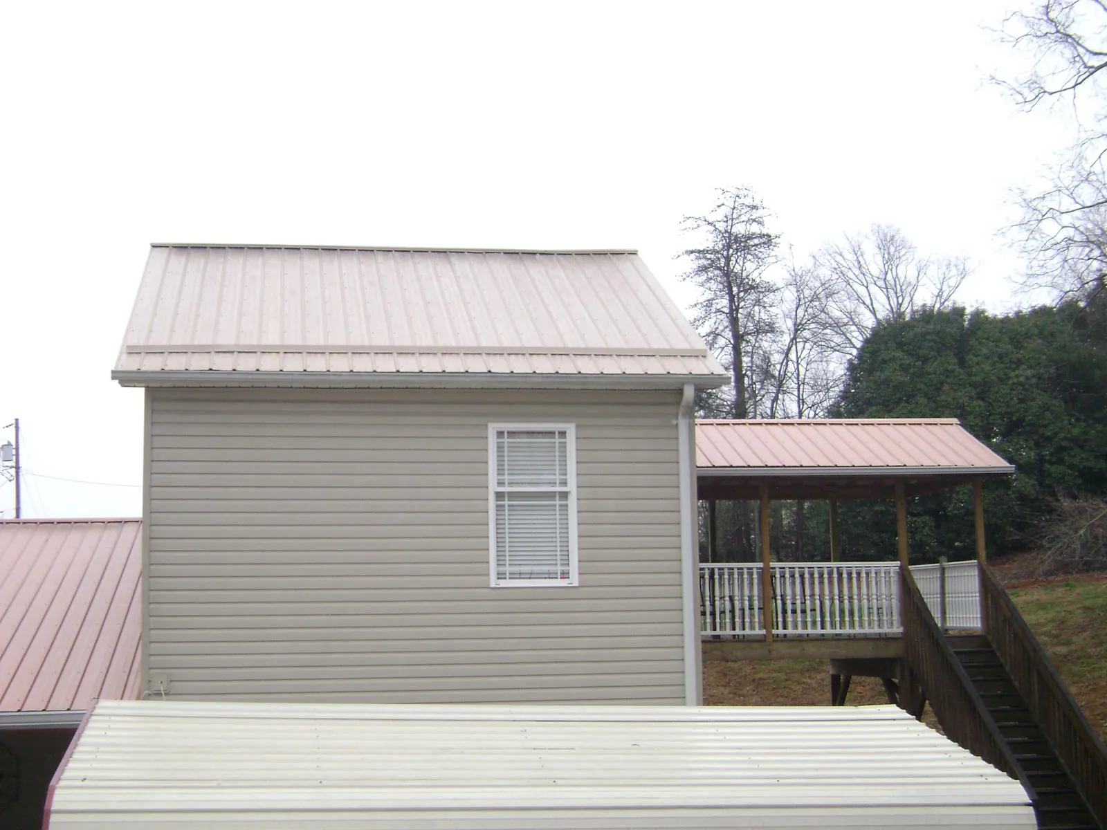 Tan metal roofs on a two story addition and attached porch, from a Roof Replacement job in Moravia